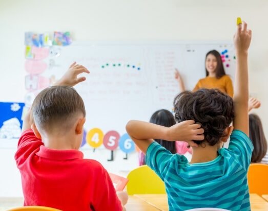 Preschool kid raise arm up to answer teacher question on whiteboard in classroom,Kindergarten education concept.
